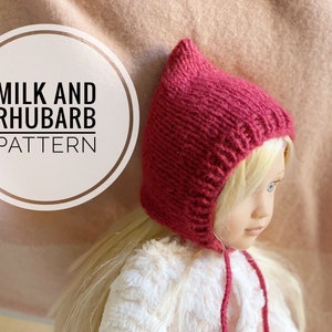 May include: A close-up of a red knitted doll hat with a pointed top and a tie. The hat is worn by a doll with blonde hair. The text "MILK AND RHUBARB PATTERN" is visible in a white circle.