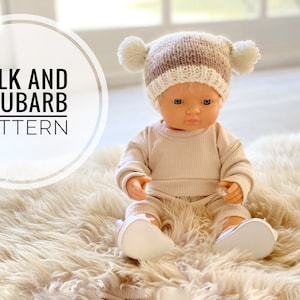May include: A knitted doll hat with pom poms in brown and white colours. The hat is on a doll wearing a beige outfit. The text "MILK AND RHUBARB PATTERN" is in a circle in the background.