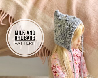 Könnte beinhalten: Eine graue Strickmütze mit spitzer Spitze und strukturierten Noppen. Die Mütze hat Bänder, die unter dem Kinn gebunden werden können. Die Mütze heißt "Milk and Rhubarb Pattern".