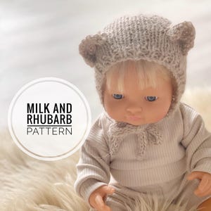 May include: A knitted doll hat with bear ears in a light beige colour. The hat is worn by a doll with blonde hair and a beige outfit. The text "Milk and Rhubarb Pattern" is visible in the image.