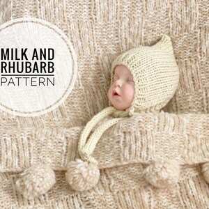 May include: A baby wearing a cream-colored knitted hat with a pom-pom on top, lying on a cream-colored knitted blanket with pom-poms. The blanket has a woven texture. The text "MILK AND RHUBARB PATTERN" is in a white circle on the blanket.