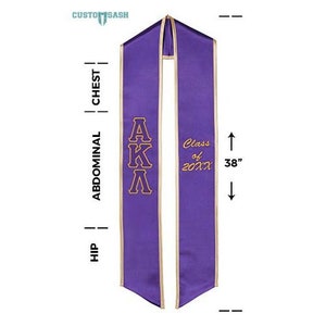 May include: Purple graduation sash with gold trim and the letters "AKA" in gold embroidery. The sash also has the text "Class of 20XX" in gold embroidery. The sash is 96.5 cm long.