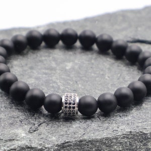May include: A black matte beaded bracelet with a silver spacer bead featuring small black cubic zirconia stones.