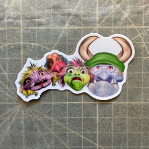 May include: Five colourful monster faces with different expressions. The monster on the right has horns and a green hat. The monster on the left has purple fur and yellow hair. The other three monsters have green, pink, and red skin.