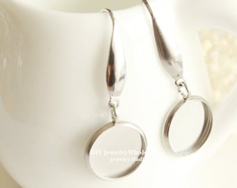 Può includere: Un paio di basi per orecchini in argento con un cerchio rotondo aperto nella parte inferiore. Gli orecchini sono appesi a una superficie bianca.