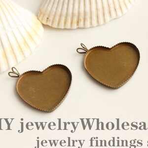 May include: Two heart-shaped brass pendant trays with scalloped edges and small loops for attaching to a chain. The trays are empty, ready for filling. The image also shows two seashells and the text "DIY jewelry Wholesale jewelry findings supplies."