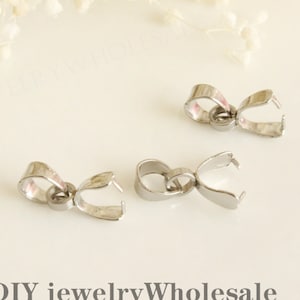 Puede incluir: Tres cierres de joyería de metal plateado, también conocidos como baúles de colgantes, se muestran sobre una superficie blanca. Estos cierres se utilizan para sujetar colgantes a collares o pulseras.