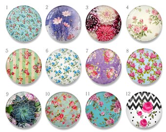 Puede incluir: Una colección de doce cabujones redondos de vidrio con varios diseños florales y estampados. Los cabujones presentan imágenes de flores, rayas y patrones geométricos en una variedad de colores, incluyendo rosa, azul y morado.
