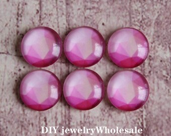 Könnte beinhalten: Sechs rosa und weiße Glascabochons mit facettiertem Design. Die Cabochons sind rund und haben eine glänzende Oberfläche.