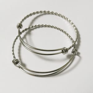 May include: Two silver bangle bracelets, one with a twisted design and the other with a smooth finish.