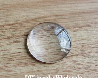 May include: A clear glass cabochon, a round, flat piece of glass with a domed top, used in jewelry making.