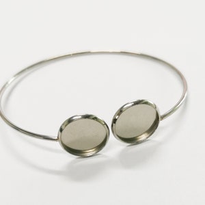 May include: Silver bangle bracelet with two round, silver-toned, bezel settings. The settings are empty and ready to be filled with a cabochon.