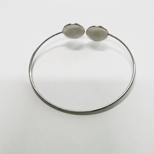 May include: A silver bangle bracelet with two round, flat, silver charms.