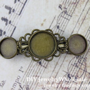 May include: A vintage bronze-coloured barrette with three circular settings for jewellery making. The central setting is larger and framed by an ornate, openwork design. The barrette has the text "ESALE" on one side.