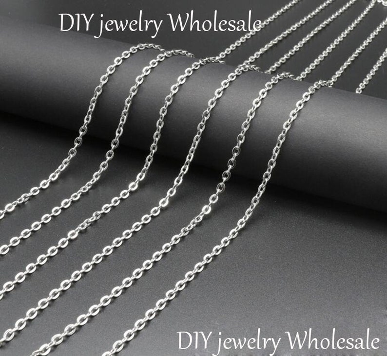 May include: A variety of silver chain links in different lengths, laid out on a black surface. DIY jewelry wholesale.