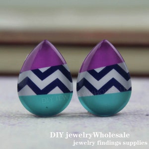 Può includere: Due cabochon in resina a forma di goccia con un motivo a chevron bianco, blu navy e turchese. I cabochon sono di colore viola chiaro nella parte superiore e sfumano in turchese nella parte inferiore.
