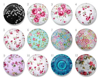 Puede incluir: Una colección de doce cabujones redondos de vidrio con varios diseños decorativos. Los diseños incluyen patrones florales en rosa, rojo y azul, un patrón floral en blanco y negro y un diseño de mandala azul. Adecuados para la fabricación de joyas o proyectos de manualidades.