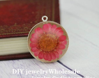 Op de afbeelding: Een zilveren hanger met een ronde, heldere harscabochon met een geperste roze bloem. De bloem heeft een gele kern en is omgeven door een zilveren bezel.