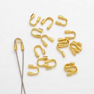 Puede incluir: Una colección de cuentas de crimpado de metal dorado para la elaboración de joyas. Las cuentas tienen forma de bucle con una pequeña abertura en la parte superior. Hay 18 cuentas en total.