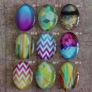 May include: Nine oval-shaped glass cabochons with different colorful patterns. The cabochons are arranged in three rows of three. The cabochons have a variety of patterns, including geometric shapes, stripes, and zigzags.
