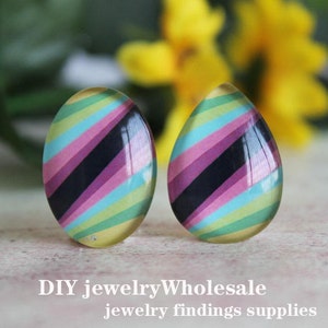 Puede incluir: Dos cabujones de vidrio de forma de lágrima coloridos con un patrón a rayas en tonos de rosa, azul, verde y negro. Los cabujones son perfectos para la elaboración de joyas.