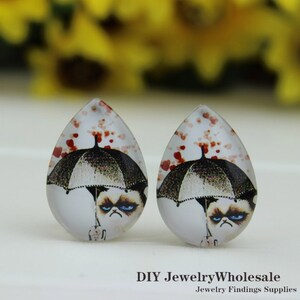May include: Two teardrop earrings with a grumpy cat design under a black and white umbrella. The earrings have a white background with red heart accents. The text "DIY JewelryWholesale" and "Jewelry Findings Supplies" is at the bottom.