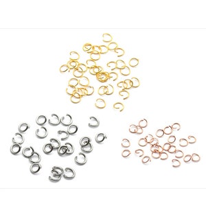 May include: A collection of jump rings in three different colours: gold, silver, and rose gold. The jump rings are scattered on a white surface.