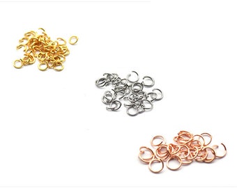 May include: Three piles of jump rings in gold, silver, and rose gold. The jump rings are small and round, and they are perfect for jewelry making.