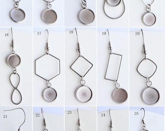 May include: A collection of silver-toned metal earrings in various geometric and organic shapes. Designs include circles, ovals, diamonds, and crosses, each with a circular base for attaching a decorative element. The earrings are displayed against a white background.