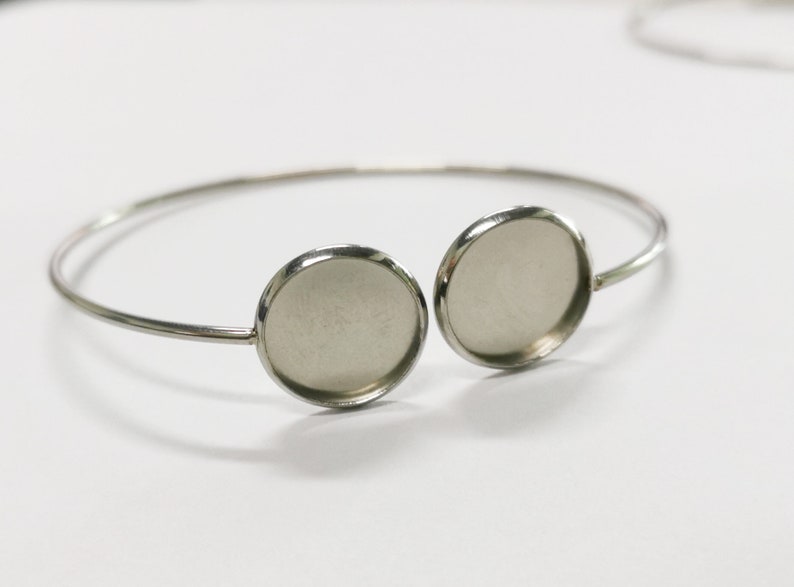 May include: Silver bangle bracelet with two round, silver-toned, bezel settings. The settings are empty and ready to be filled with resin or other materials.
