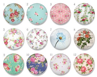 Puede incluir: Una colección de doce cabujones redondos de vidrio con diseños florales. Los cabujones presentan varios patrones, incluyendo rosas, margaritas y notas musicales, en tonos de rosa, azul y blanco. Estas piezas de vidrio decorativas son ideales para manualidades.