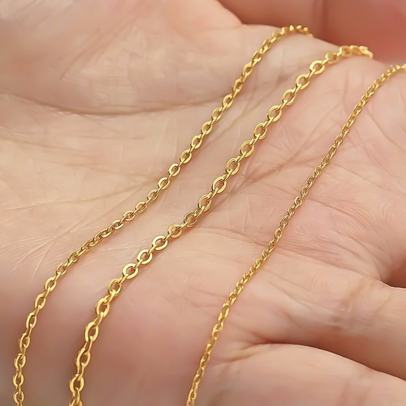 May include: Three gold chains of different lengths and thicknesses, displayed on a hand.