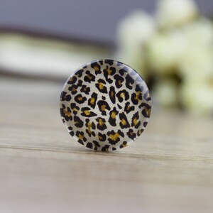 May include: A round, white button with a brown and black leopard print design.