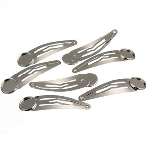 May include: A collection of silver-toned metal hair clips with a flat, oval base for attaching embellishments. The clips are curved and have a classic snap closure design, perfect for DIY hair accessories.