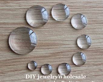 May include: Assortment of clear glass cabochons of various sizes, arranged in a circle on a wooden surface. DIY jewelry wholesale, jewelry findings supplies.