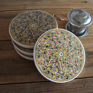 May include: Set of four yellow ceramic coasters with a black and red floral design. The coasters are round and have a raised edge.