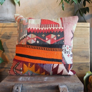 May include: A colourful patchwork cushion with a geometric design in shades of red, orange, black, and white. The cushion is made of woven fabric and has a fringed edge.