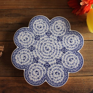 May include: A white ceramic trivet with a blue and white floral pattern. The trivet is shaped like a flower with eight petals.