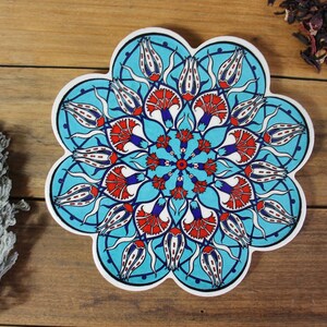 May include: A blue and white ceramic trivet with a floral design. The trivet is shaped like a flower with 12 petals. The design features red, white, and blue flowers with intricate details.