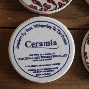 K&ouml;nnte beinhalten: Wei&szlig;er Keramikuntersetzer mit blauem Text, der "Inspired By Past, Whispering To The Future, Ceramia" lautet. Der Text setzt sich fort mit "This work is a sample of Traditional Iznik Turkish Ceramic Art of the 16-18th Century. Lead Free Glazed & Heat Resisted. Original Registered Product. All Rights Reserved. Made in Turkey."