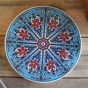May include: A round blue and white ceramic plate with a red and white floral design. The plate has a decorative border with a repeating pattern.