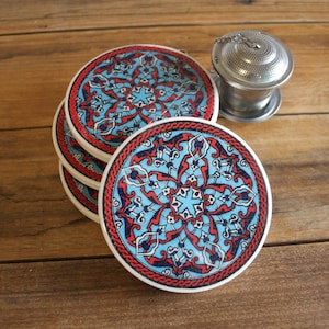 May include: Set of four blue and red ceramic coasters with intricate floral patterns. The coasters are stacked on top of each other.