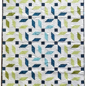 May include: A quilted blanket with a geometric pattern. The design features diamond shapes in shades of blue and green, along with small black squares, set against a white background. The quilt has a textured appearance due to the stitching.