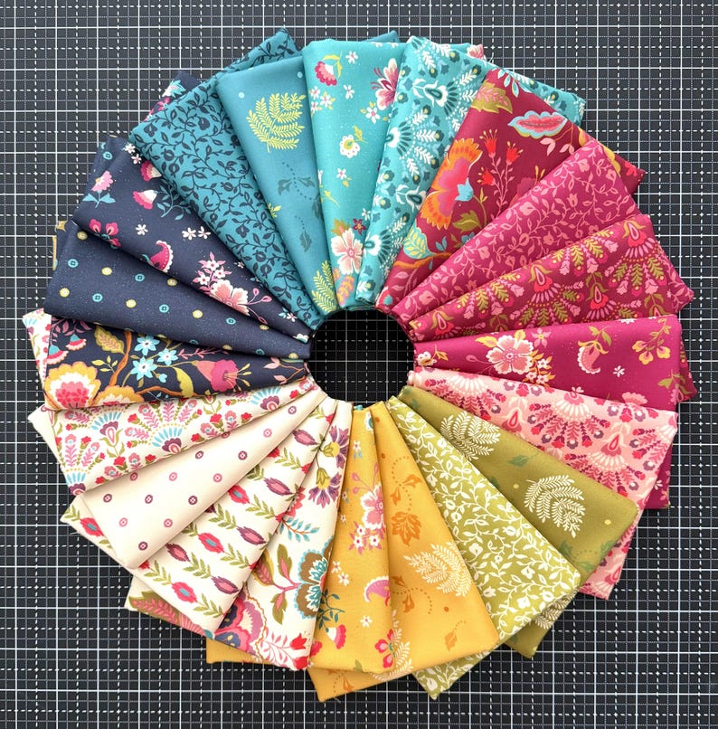 May include: A circular arrangement of folded fabric swatches featuring a variety of floral and geometric patterns in a spectrum of colors including teal, navy blue, cream, yellow, olive green, pink, and magenta, displayed in a fan-like layout.