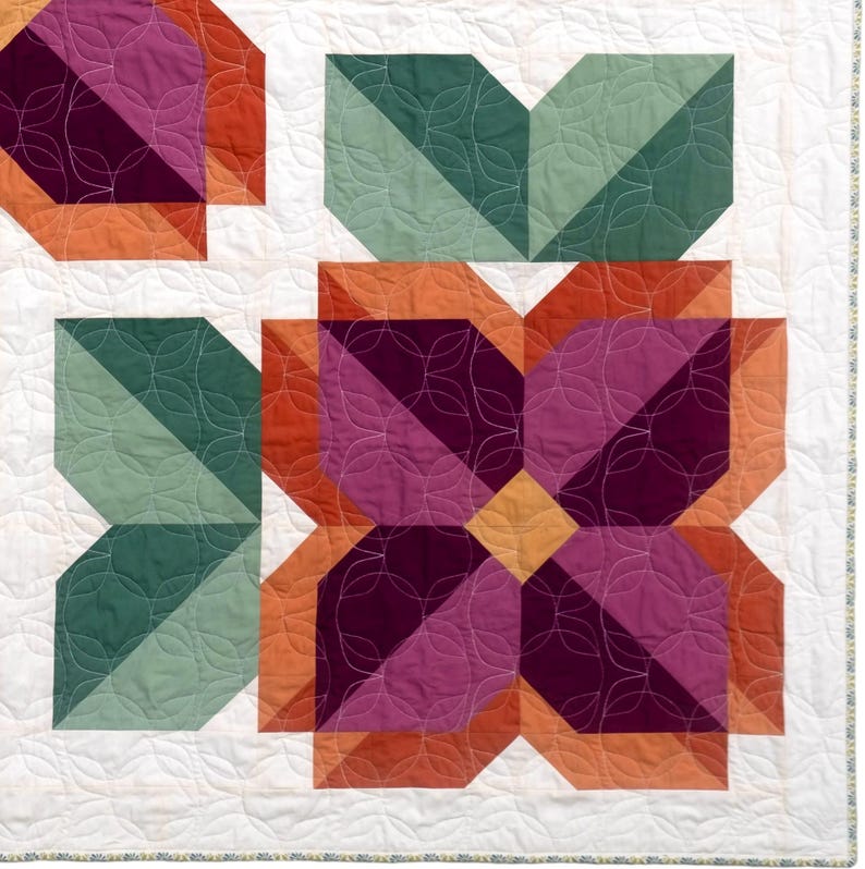 May include: A quilt featuring a floral pattern with geometric petals in shades of deep purple, magenta, and orange, accented by sage green leaves. The white background is stitched with a repeating circular pattern, and the edge has a thin floral border.