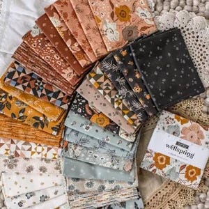 May include: A collection of square fabric swatches arranged in a fan pattern, featuring various floral, geometric, and botanical prints in shades of terracotta, mustard, sage green, black, and cream. A paper band labeled Wellspring is included.