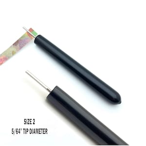 May include: Two black paper piercing tools with a silver needle. The tool on the left is being used to pierce a piece of patterned paper. The tool on the right is shown with the needle extended. The text "SIZE 2 5/64" TIP DIAMETER" is printed below the tools.