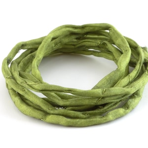Può includere: Un rotolo di nastro di seta verde, avvolto in un cerchio. Il nastro è morbido e ha una lucentezza delicata.
