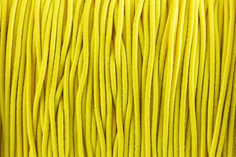 May include: Close-up of a spool of bright yellow elastic cord. The cord is tightly wound and has a smooth, consistent texture.