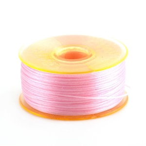 May include: A spool of pink thread wound around a yellow plastic bobbin.